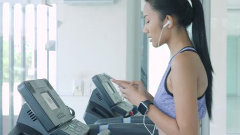 asian girl running on the treadmill in the gym with earphones