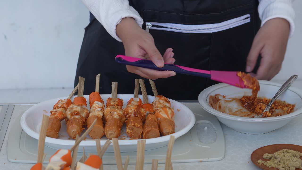 Donna in grembiule che spalma spezie e salsa sul Suki Satay prima di grigliare