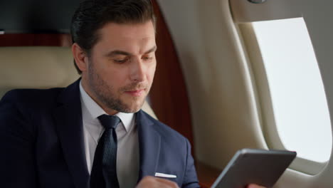 Stylish-manager-using-pad-computer-in-airplane-closeup.-Smiling-man-flying-first