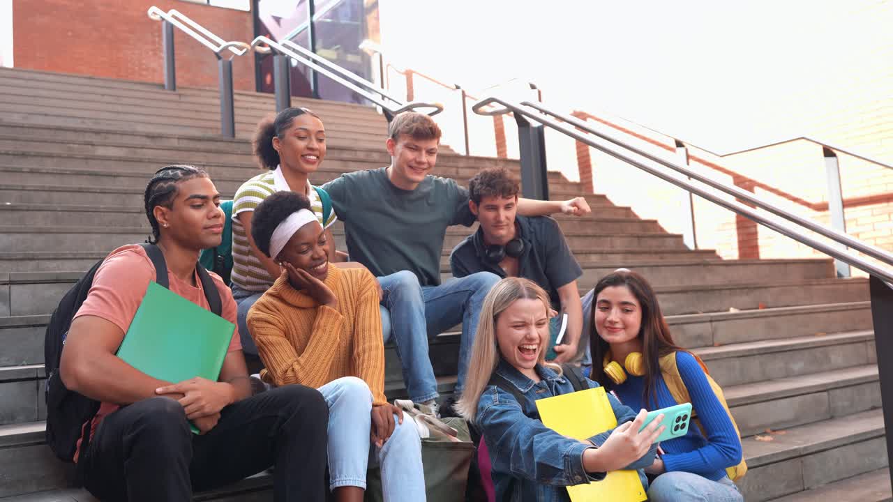 Mangfoldig gruppe glade studenter tar en selfie på campustrappen.