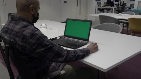 vista sobre el hombro de un hombre casual inteligente que usa una máscara facial que trabaja en una computadora portátil
