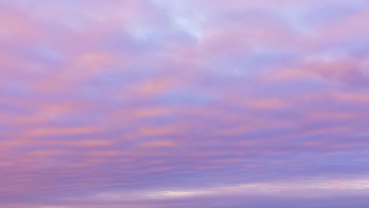 Wide panoramic sky with thin layered clouds changing color from warm peach and pink near horizon to cool lavender, blue and indigo above, creating serene atmospheric backdrop, with sky, cloud, pastel