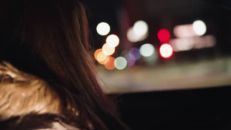 perspectiva en primera persona de una dama en un coche bajando el vidrio de la ventana por la noche, capturada con una cámara de mano. el fondo presenta luces de la ciudad coloridas y borrosas