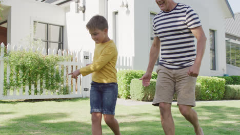 Glücklicher-Kaukasischer-Großvater-Und-Enkel-Spielen-Fußball-Im-Garten,-Zeitlupe