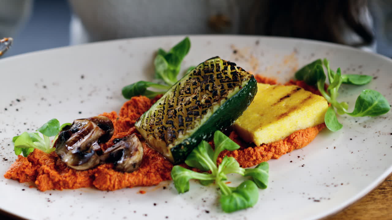 Woman eating grilled zucchini with mushrooms, polenta and hummus