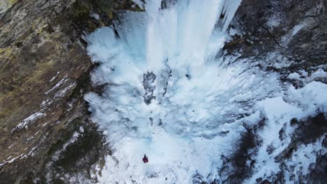 Aerial-view-of-a-waterfall-with-a-mountaineer-standing-in-front-of-it