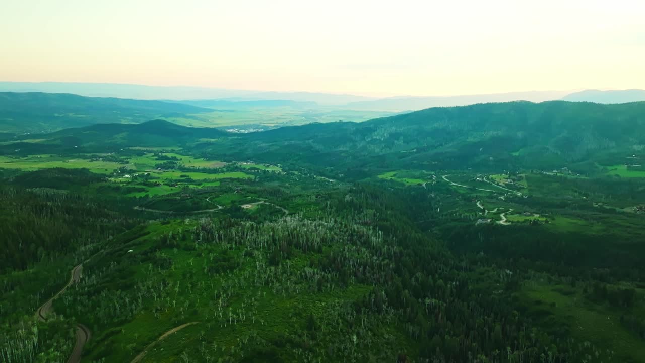 Golden hour drone over Steamboat Springs hills with expansive of forested terrain, panoramic aerial backdrop