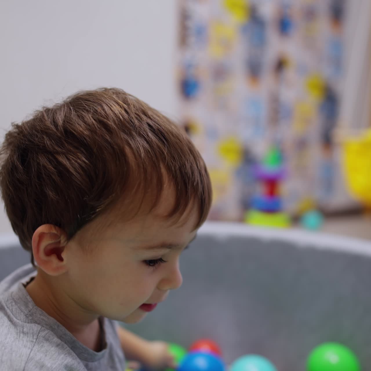 Un neonato sdraiato nella piscina asciutta si tira su. Un bambino adorabile lancia la palla in avanti. Sfondo sfocato