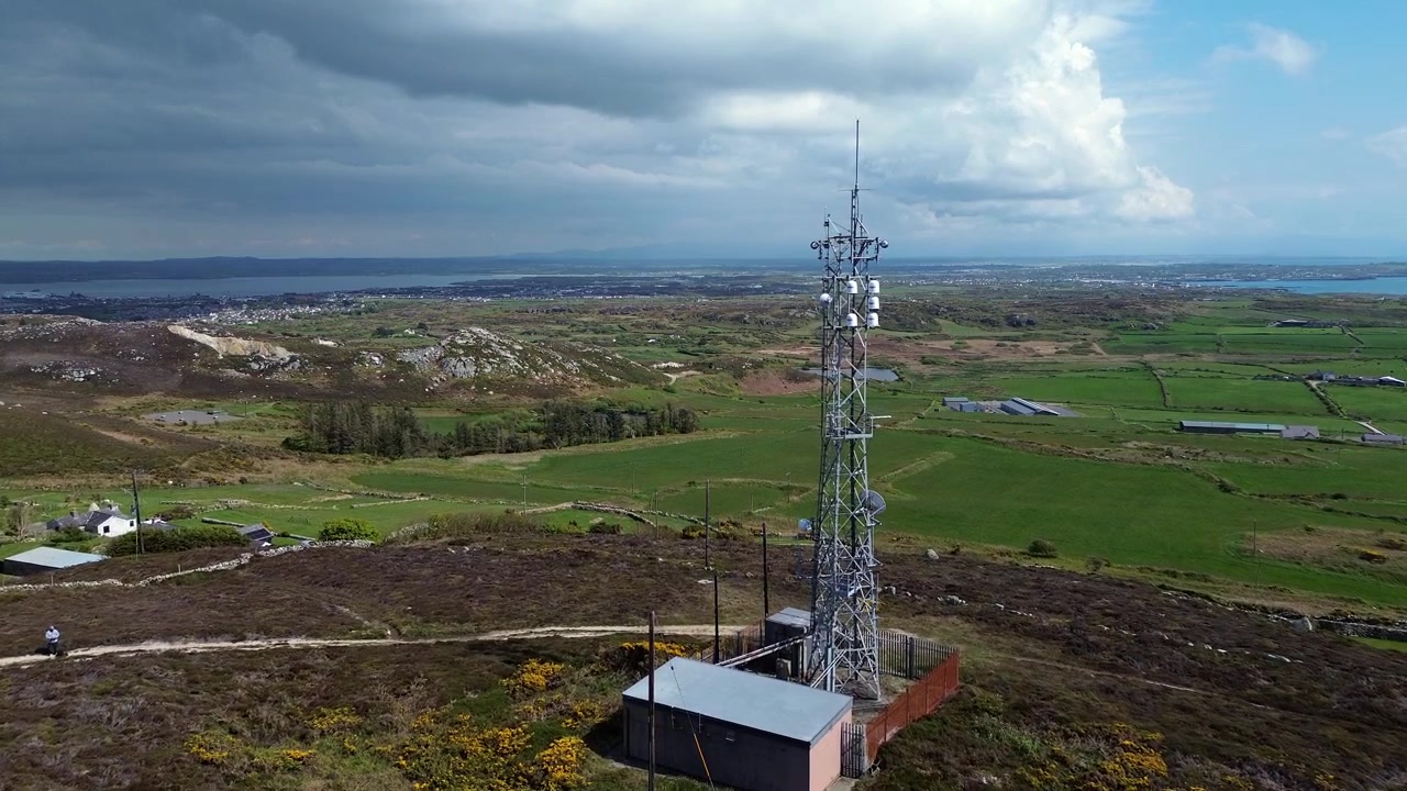 Vista aérea de la antena de telecomunicaciones de la montaña Holyhead acercándose al paisaje marino rural de la isla galesa
