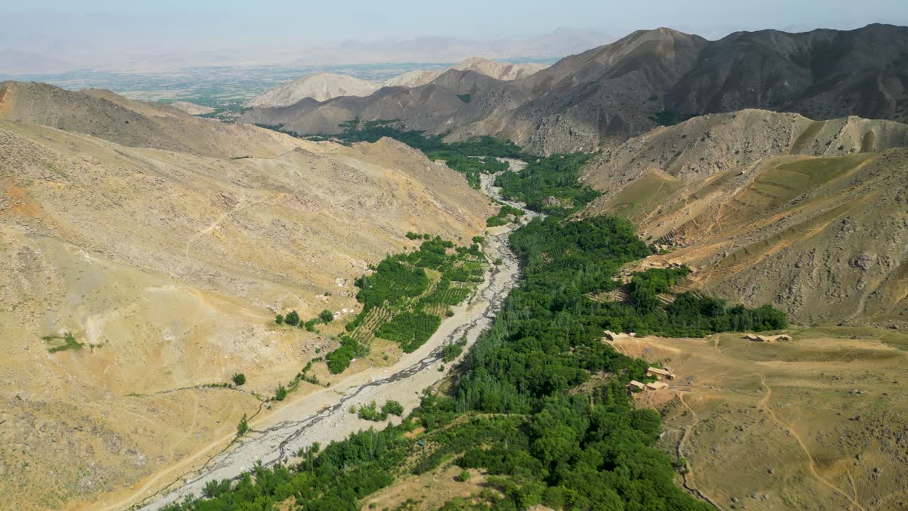 Aerial drone view of a river winding through a green lush, rugged mountain valley in Kabul, Afghanistan