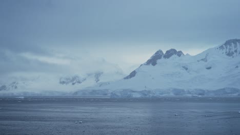 Winter-Mountains-and-Glacier-on-Coast,-Coastal-Mountain-Scenery-in-Antarctica,-Cold-Blue-Landscape-and-Seascape-with-Glacier-Ice-and-Ocean-Sea-Water,-Antarctic-Peninsula-Dramatic-Coastline-Scene