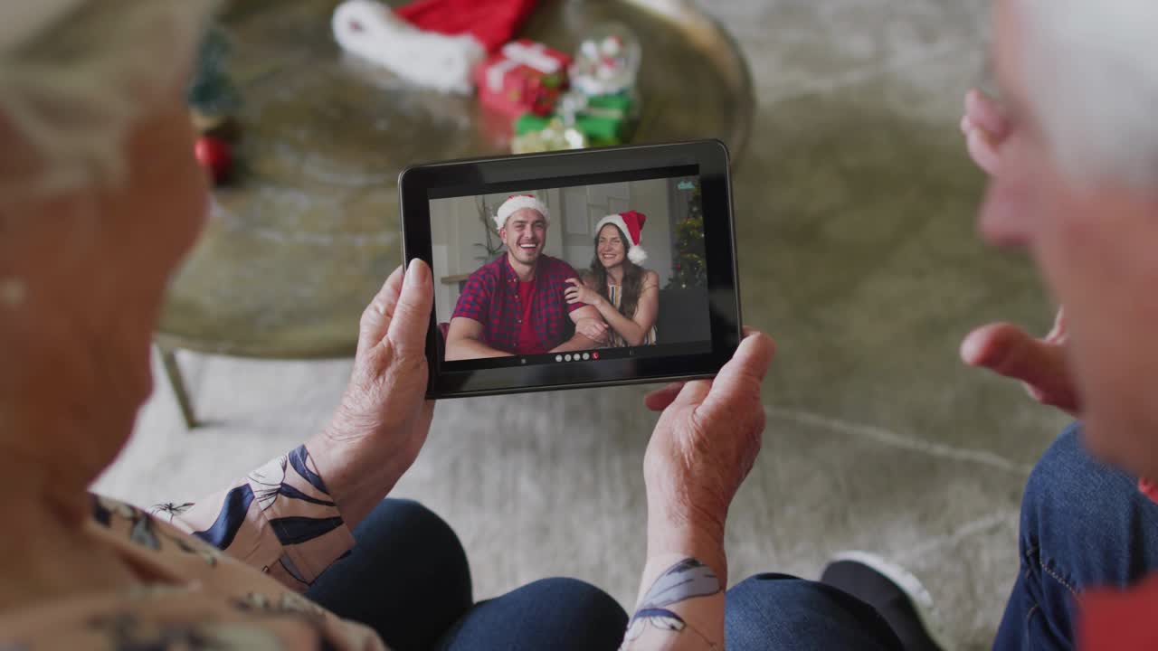 Una coppia di anziani che tiene in mano un tablet guarda una famiglia che saluta, mentre un'interfaccia utente tecnologica AR si forma sulle mani collegando i parenti