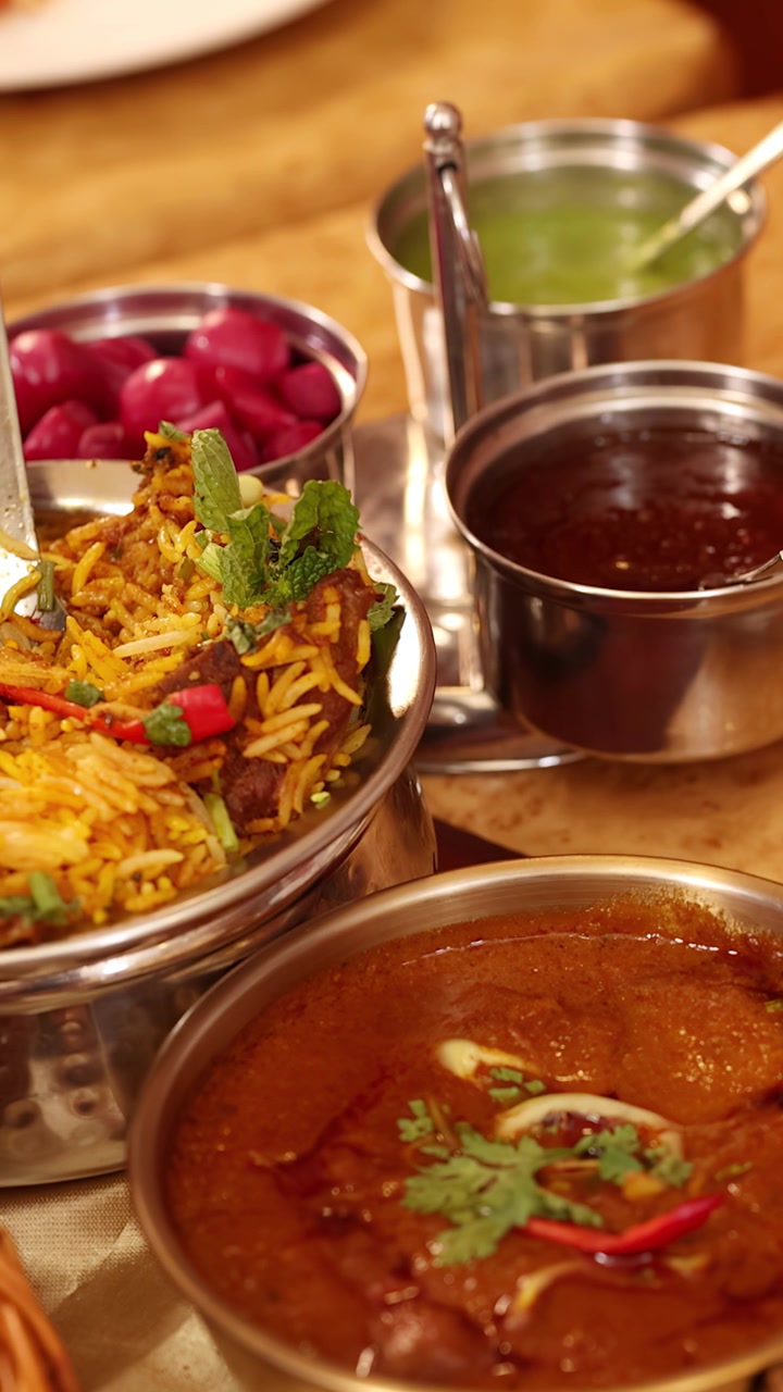 Nærbillede af forskellige indiske retter, herunder krydret biryani, tandoori kylling og karry, på et restaurantbord.