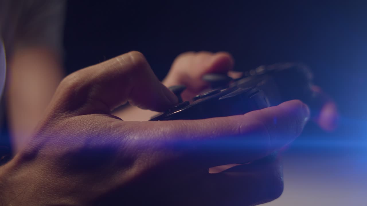 Playing video games in a darkened room with an anamorphic lens flare on a small controllers buttons playing quickly close up