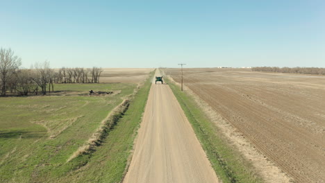 tractor sprayer driving on the dirt road beside the agricultural land on a sunny day in saskatchewan, canada