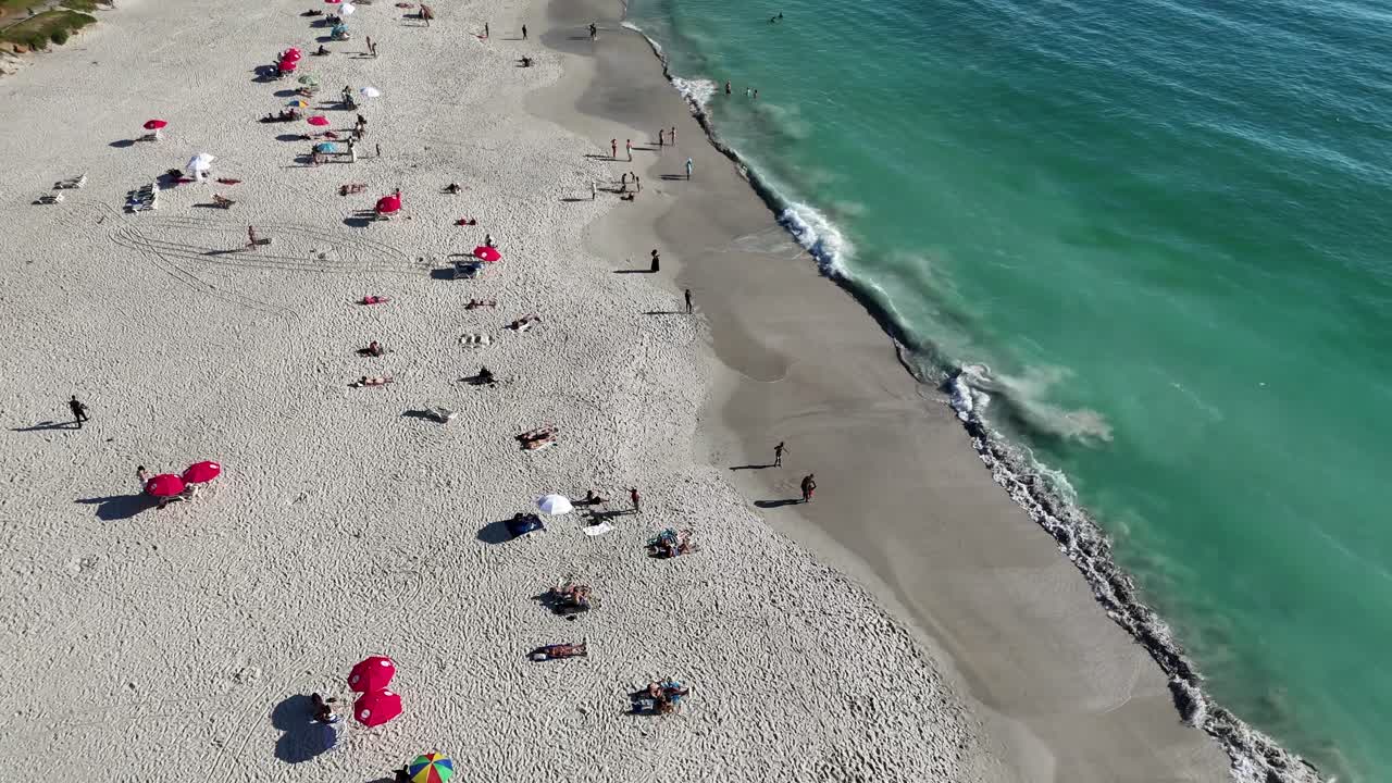 Aerial top down of tourist sunbathing with umbrella and swimming in Atlantic ocean in South Africa