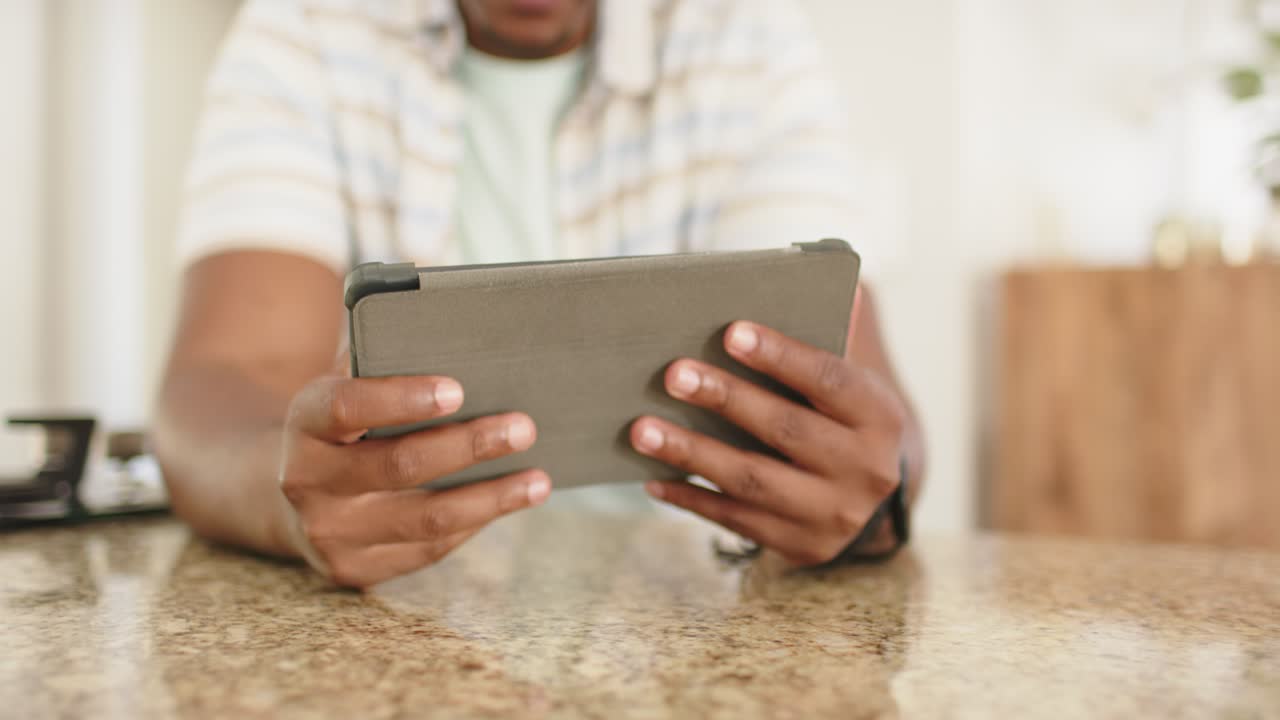 Adult male African American noticing screen at granite counter tapping and swiping tablet to read