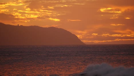 a ave rolls in as the sun sets over kaena point hawaii oahu north shore with purple and orange as the predominant colours