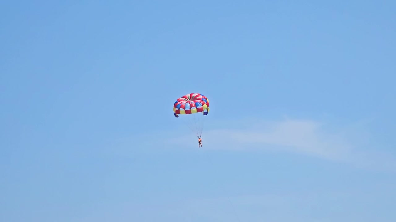 Person, der parasailer højt oppe i den klare, blå himmel og oplever et spændende sommer eventyr, spænding og frihed under vandsportsaktiviteten som en del af en sjov strandferie i Da Nang, Vietnam