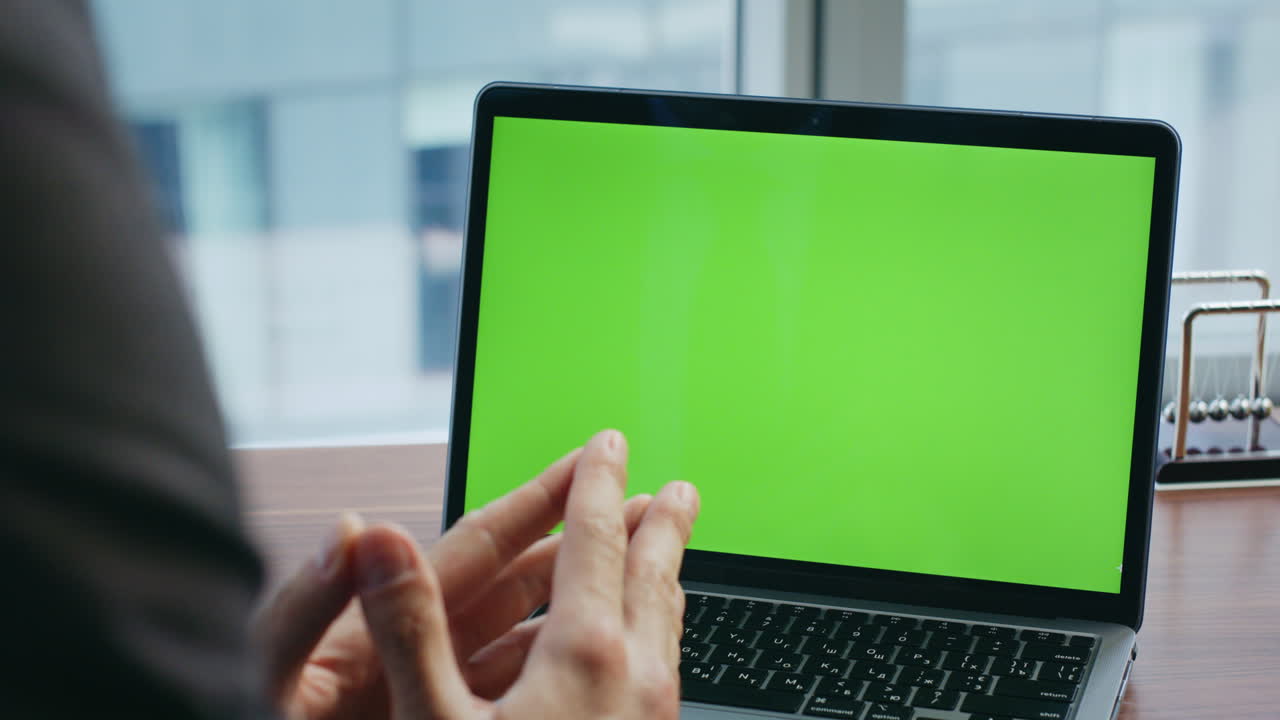 un hombre de negocios llamando por video a un portátil de pantalla verde sentado en una oficina de lujo de cerca.