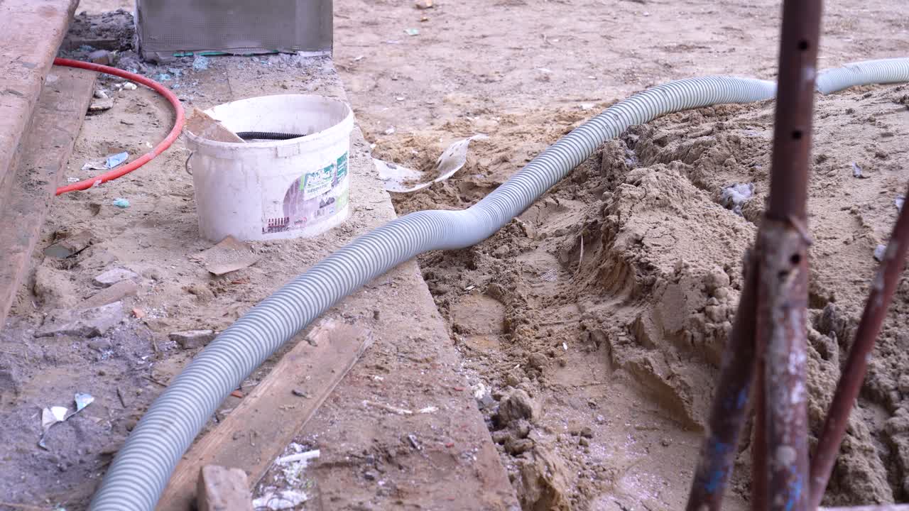 Flexible gray hose lies in construction sand next to scattered building debris