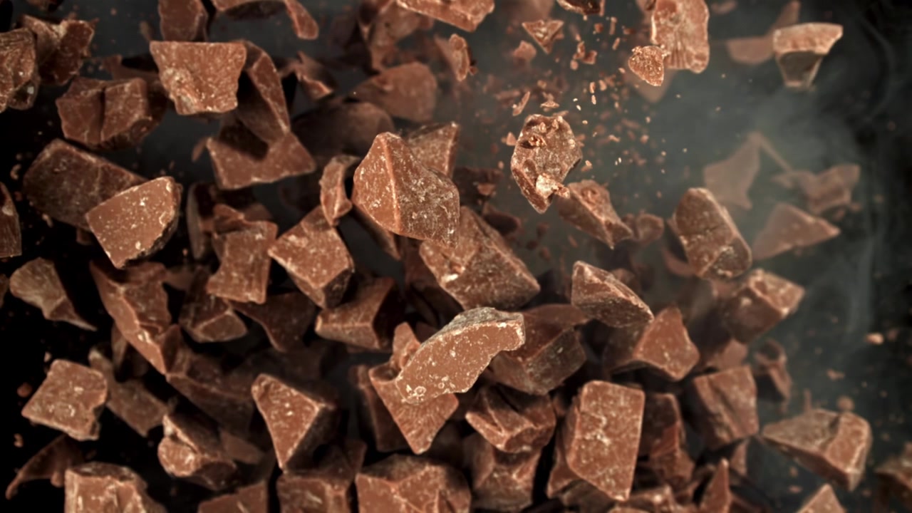 Super rallentatore di pezzi di cioccolato che cadono con polvere di cacao