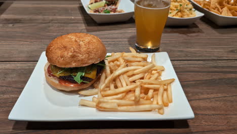 close-up of burger and fries with a beer on a wooden table