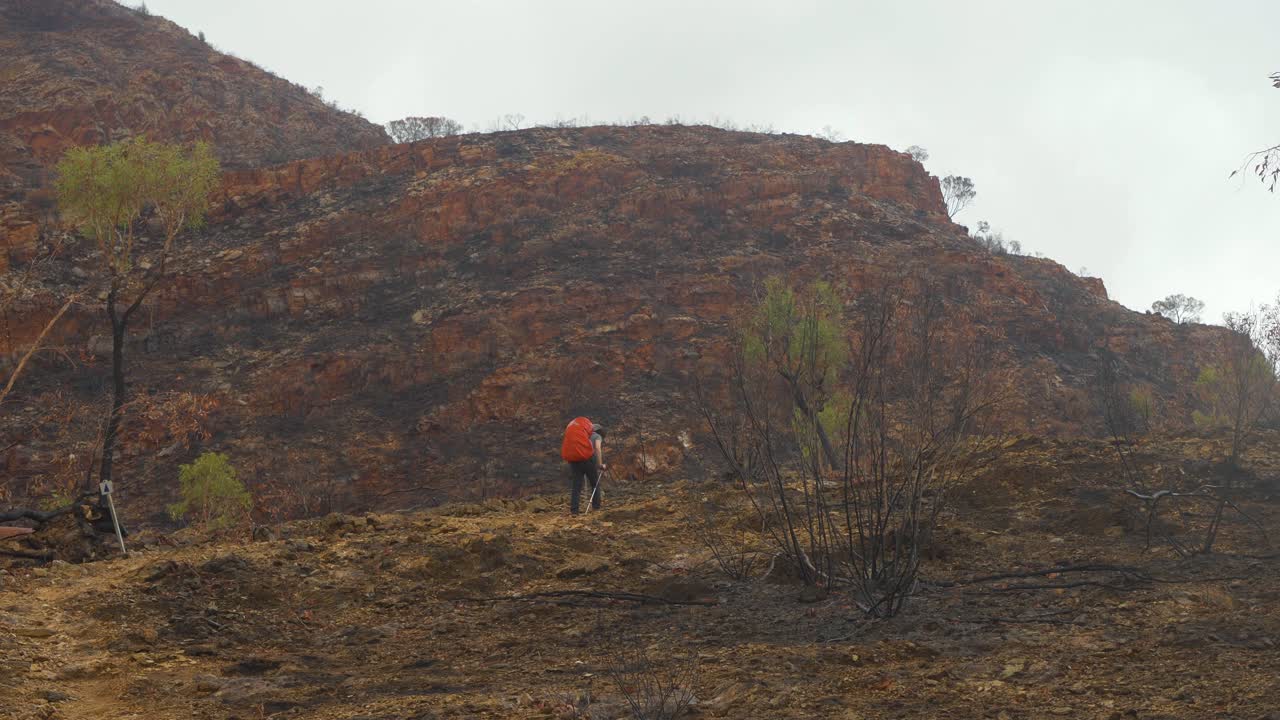 un excursionista camina a través de una zona rocosa y dañada por el fuego, en el centro de australia