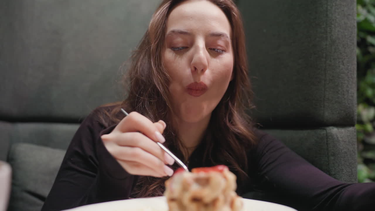 Lady sits in cozy booth enjoying waffles with smile, nodding with delight before sipping latte. Scene captures joyful moment of relaxation and satisfaction during breakfast in warm indoor cafeteria