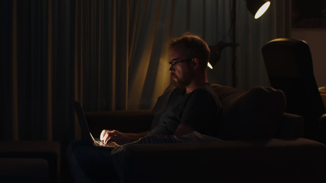 A workaholic man works on his laptop late at night and slowly looks up