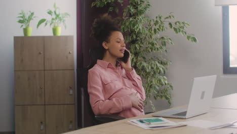Pregnant-Woman-Talking-On-Her-Mobile-Phone-And-Caressing-Her-Belly-While-Working-In-The-Office-1