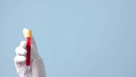 mano con guante médico sosteniendo una muestra de sangre sobre fondo azul con espacio de copia, cámara lenta