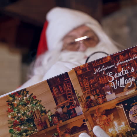 portrait of santa with a book. santa claus with white beard in eyeglasses looking into the magic book indoors. close-up. christmas time.