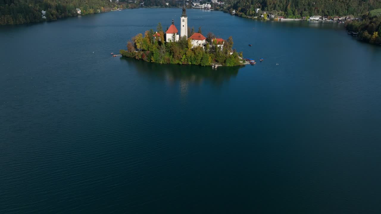 Ripresa aerea con tilt up che rivela la Chiesa dell'Assunta sull'isola del Lago di Bled con montagne alpine in Slovenia.