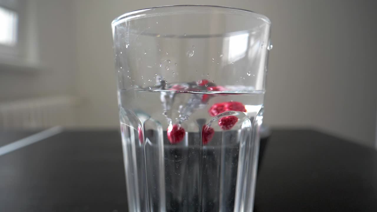 냉동 라즈베리는 느린 동작으로 물과 함께 유리에 떨어집니다.