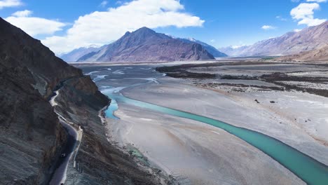 aerial drone shot displaying a vehicle crossing a bridge over the river in nubra valley, framed by natural beauty.