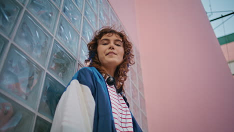 curly hipster posing urban area looking camera close up. woman leaning on wall