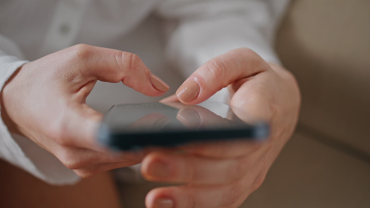 Lady fingers touching smartphone touchscreen browsing app at apartment closeup