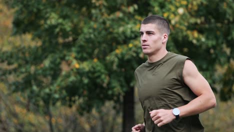 male sporty jogger with smartwatch monitoring running through a park with trees, slow motion tracking shot