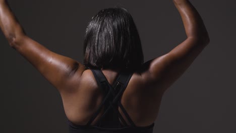 vista trasera de estudio de una mujer madura con ropa de gimnasia haciendo ejercicio con palos de artes marciales escrima