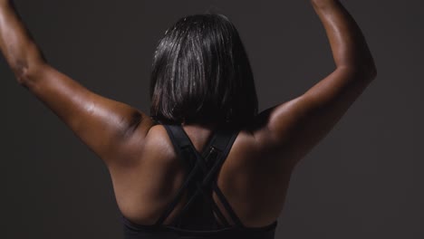 rear view studio shot of mature woman wearing gym fitness clothing exercising with martial arts escrima sticks