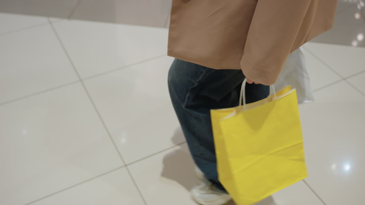 가방을 자연스럽게 흔들면서, 반짝이는 타일을 지나 가방을 들고 걷고, 청바지를 입고 가방을 흔들며 쇼핑몰을 거닐고, 핸드백을 흔들며 편안한 옷차림으로 조명이 켜진 상점 앞을 어슬렁거립니다.