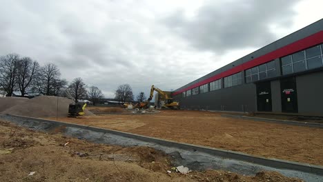 Bagger-Arbeitet-Auf-Der-Baustelle-Einer-Halle-Vor-Wolkenhintergrund