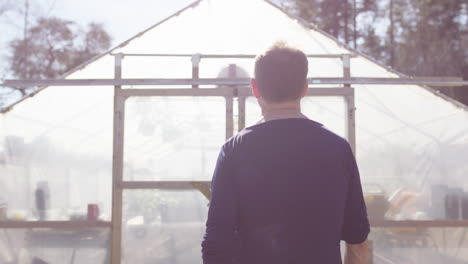 man walks up and open greenhouse doors in bright daylight, rear slomo tracking