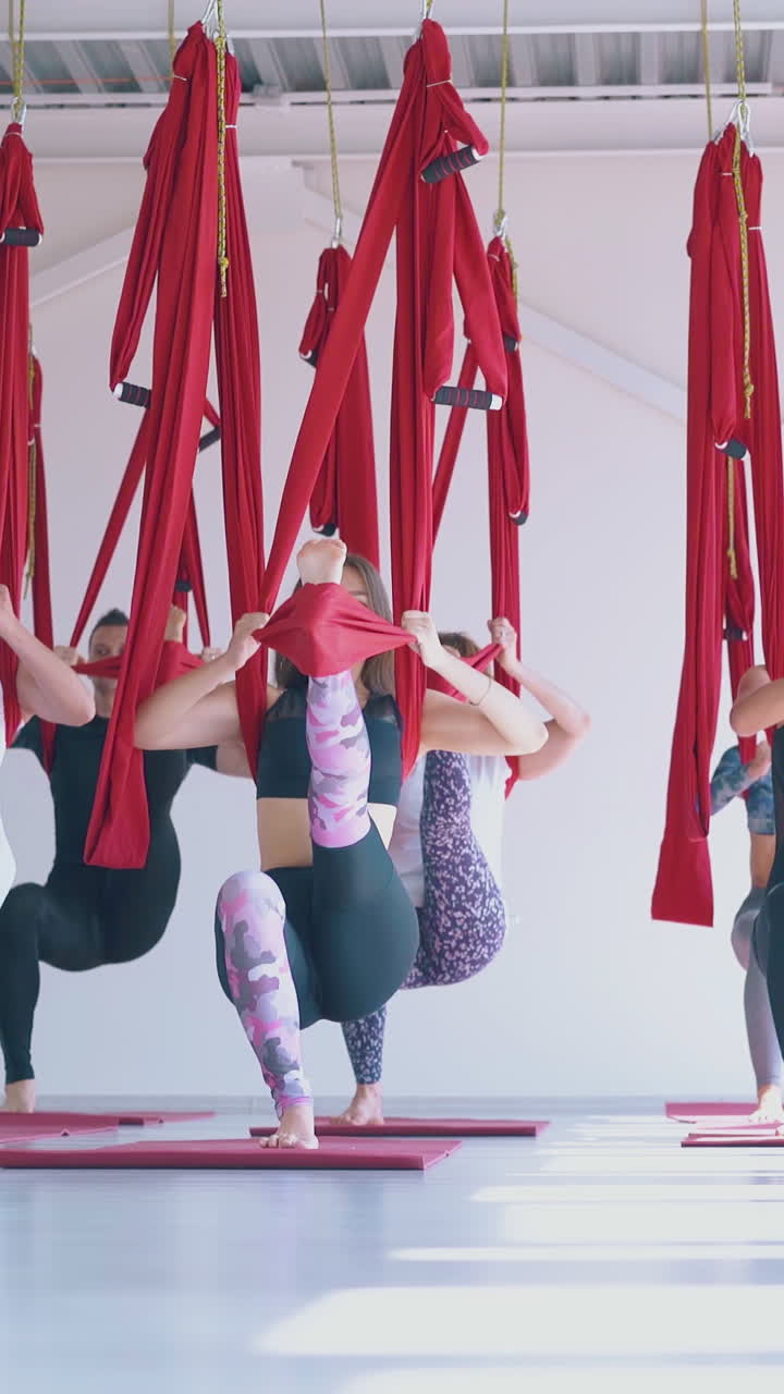relaxed women group practices modern pilates with long red hammocks and stand concentrated in yoga asana