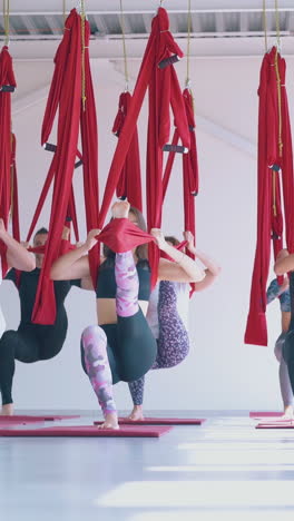 relaxed women group practices modern pilates with long red hammocks and stand concentrated in yoga asana