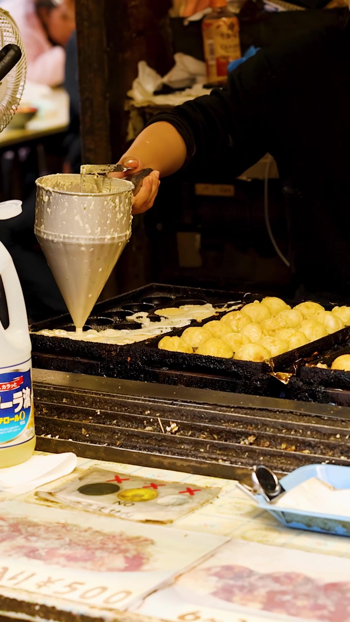 Un venditore versa la pastella in una piastra calda per takoyaki in una bancarella di strada a Tokyo.