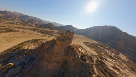 Epic-FPV-aerial-flying-fast-around-a-rocky-butte-in-a-hot,-arid-desert-landscape