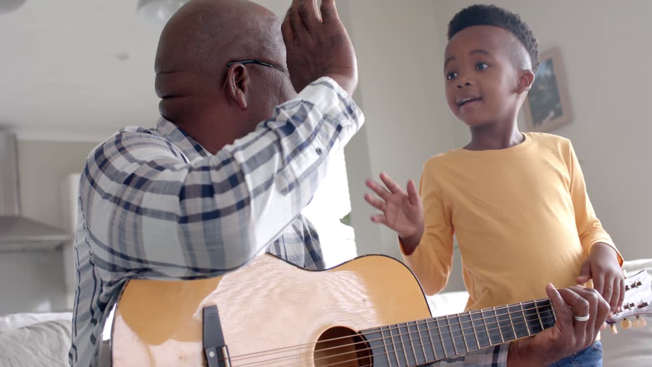Nonno e nipote afroamericani felici che suonano la chitarra e si danno il cinque a casa, al rallentatore