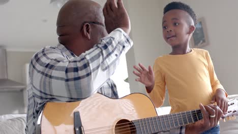 Feliz-Abuelo-Y-Nieto-Afroamericano-Tocando-La-Guitarra,-Chocando-Los-Cinco-En-Casa,-Cámara-Lenta